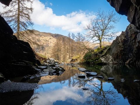 Stepping stones crossing the still pool inside Rydal Cave, reflecting bare trees and blue sky